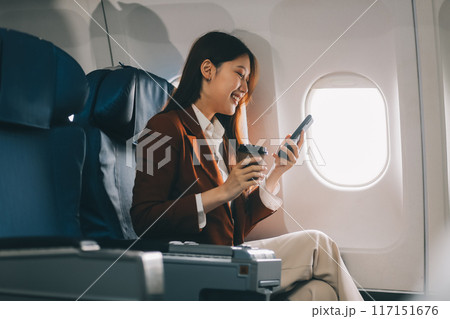 .Asian woman looking at phone while sitting on airplane Technology female travelers using mobile smartphones, online apps, and the internet while sitting in airplane seats during travel. 117151676
