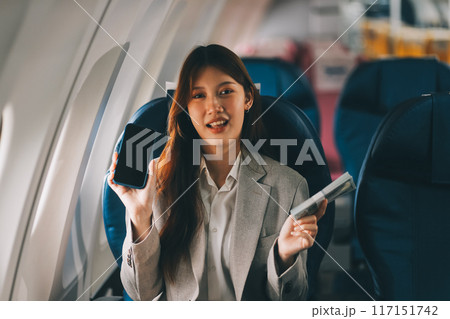 A young Asian woman, seated as an airplane passenger, contemplates dollar bills, reflecting on lucrative opportunities and aspirations towards billionaire status. A young Asian woman, seated as an airplane passenger, contemplates dollar bills, reflecting on lucrative opportunities and aspirations towards billionaire status. 117151742