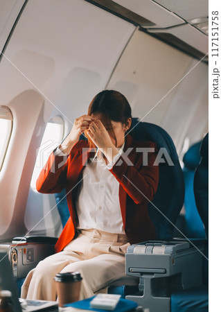 Photo of a frustrated woman sitting on an airplane with her head in her hands. Asian woman sitting in a seat in airplane Photo of a frustrated woman sitting on an airplane with her head in her hands. Asian woman sitting in a seat in airplane 117151758