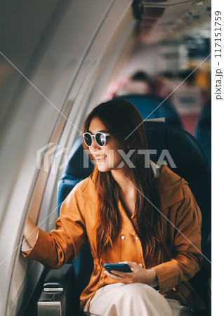 Joyful asian woman sits in the airplane and using tablet while go to travel Joyful asian woman sits in the airplane and using tablet while go to travel 117151759