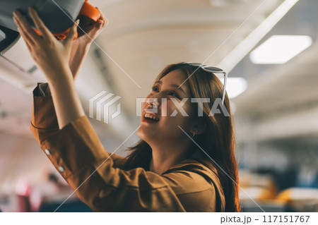 Female tourist packing her luggage in the airplane cabin. 117151767