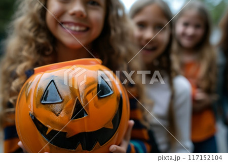 Group of joyful girls holding a carved pumpkin, smiling together outdoors 117152104