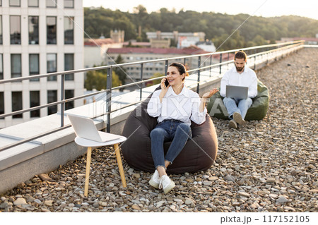 Business colleagues working outdoors on rooftop with laptops 117152105