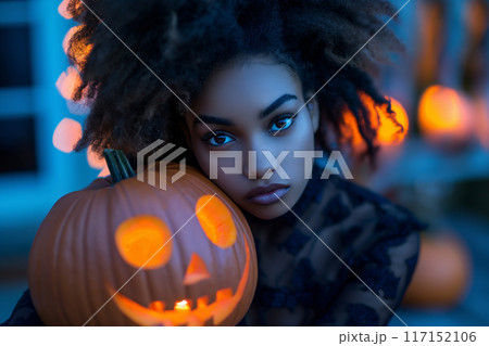 Young woman with curly hair glowing in blue light near carved pumpkins 117152106