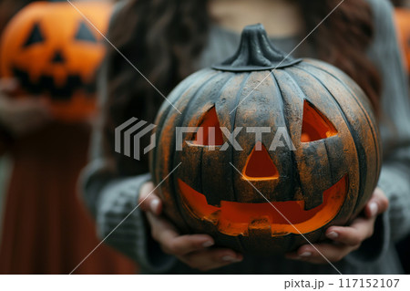 Woman holding a carved pumpkin with a haunting expression at twilight 117152107