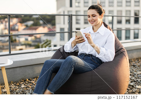 Woman relaxing on rooftop while using her smartphone Woman relaxing on rooftop while using her smartphone 117152167