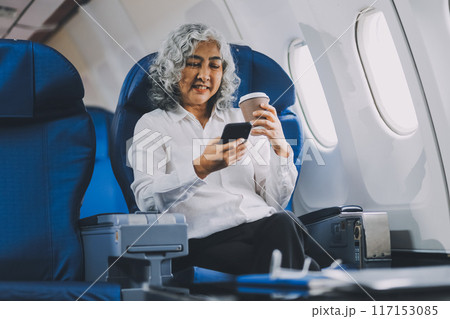 business woman sitting inside plane at the airport with sky view from the window drinking a cup of coffee 117153085