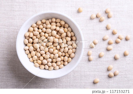 Dried soybeans, also soy beans or soya beans in a white bowl on linen fabric. Whole and raw seeds of the legume and oilseed Glycine max, with a very high protein and oil content. Close-up from above. Dried soybeans, also soy beans or soya beans in a white bowl on linen fabric. Whole and raw seeds of the legume and oilseed Glycine max, with a very high protein and oil content. Close-up from above. 117153271