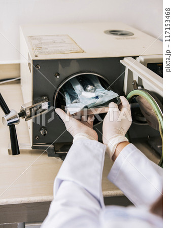 Close up of hands with dental autoclave sterilizer machine. Dentist hands sterilizing tools with autoclave, dentist with dental autoclave, close up of dentist with steam sterilizer 117153468