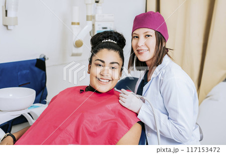 Female dentist with smiling female patient looking at camera, Professional dentist with female patient in office, Portrait of smiling dentist with female patient in medical office 117153472