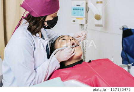 Dental specialist cleaning the teeth of a female patient. Professional dentist cleaning a female patient's mouth, Female dentist cleaning and examining a female patient's mouth 117153473