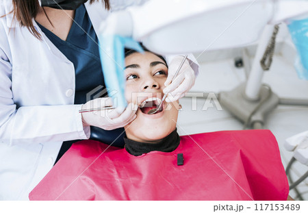 Top view of dentist doing cleaning to female patient lying down. Dentist doctor examining mouth to patient lying on chair, Female dentist examining mouth to patient lying down Top view of dentist doing cleaning to female patient lying down. Dentist doctor examining mouth to patient lying on chair, Female dentist examining mouth to patient lying down 117153489