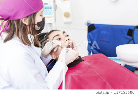 Close-up of a stomatologist cleaning a woman teeth, Stomatologist cleaning a patient's teeth, View of a dentist cleaning a patient's mouth with a drill. Stomatologist cleaning caries with drill 117153506