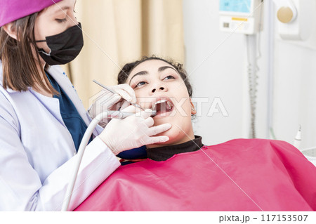 View of a dentist cleaning a patient mouth with a drill. Stomatologist cleaning a patient's teeth, Close-up of a stomatologist cleaning a woman's teeth, Stomatologist cleaning caries with drill 117153507