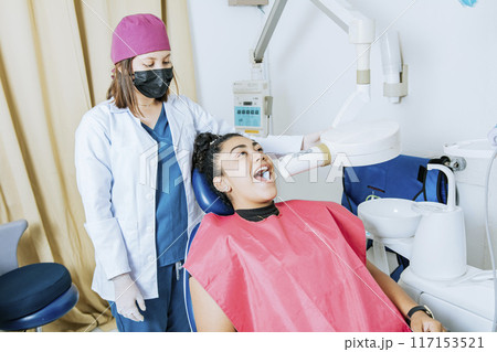 Dentist performing intraoral dental x-ray on a patient, Dentist performing intraoral x-ray assessment on a patient, a dentist performing dental x-rays in the office. Intraoral radiography concept Dentist performing intraoral dental x-ray on a patient, Dentist performing intraoral x-ray assessment on a patient, a dentist performing dental x-rays in the office. Intraoral radiography concept 117153521