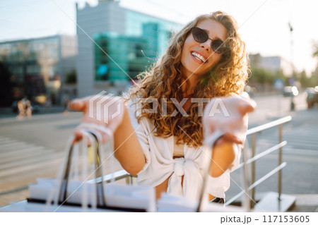 Stylish woman with shopping bags walks through city street. Consumerism, shopping, lifestyle concept 117153605