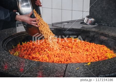 male chef adds chickpeas to a cauldron with carrots to cook traditional oriental Uzbek pilaf in asian kitchen at a restaurant in Uzbekistan 117154186