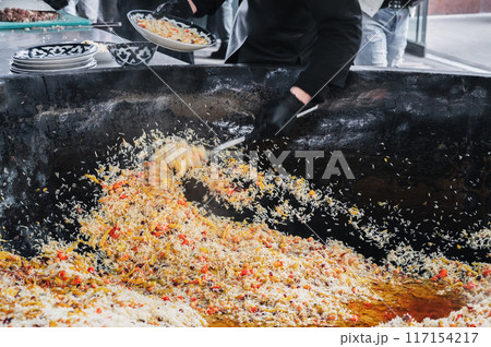 male cook cooked Uzbek pilaf from cauldron on a plate in the kitchen. Traditional Oriental Arabic cuisine. Central Asian Pilaf Center in Uzbekistan in Tashkent 117154217