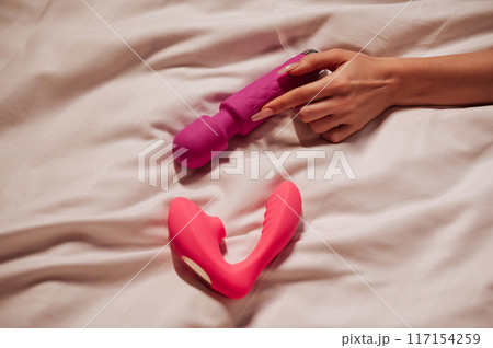 sex vibrator and vacuum stimulator in a woman girl hand on a white sheet on bed in bedroom. Sex toys for female satisfaction and orgasm 117154259