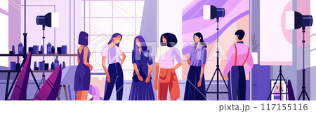 Fashion photoshoot scene with models and photographers in a studio setting with lighting equipment shelves and a large window 117155116