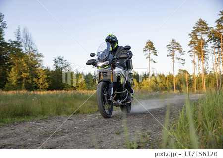Driver riding motorcycle on empty road during sunset 117156120