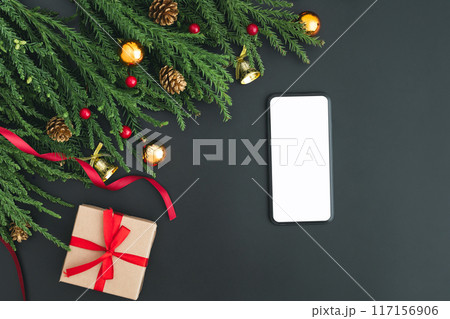 Top view of smartphone with white mock-up screen and festive decorations on the black background. 117156906