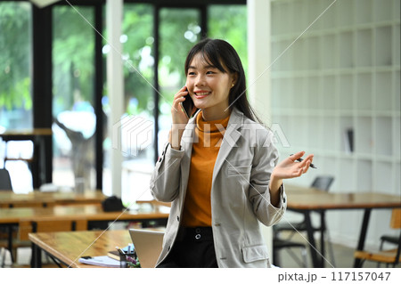 Young stylish businesswoman having pleasant phone conversation sitting at modern office 117157047