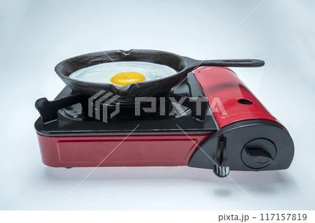 A red pan with a yellow egg in it sits on top of a red stove A red pan with a yellow egg in it sits on top of a red stove 117157819