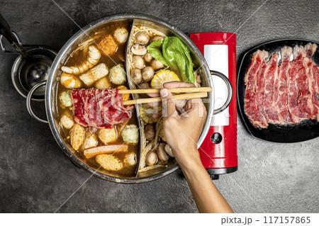 A person is eating food from a pot with chopsticks A person is eating food from a pot with chopsticks 117157865