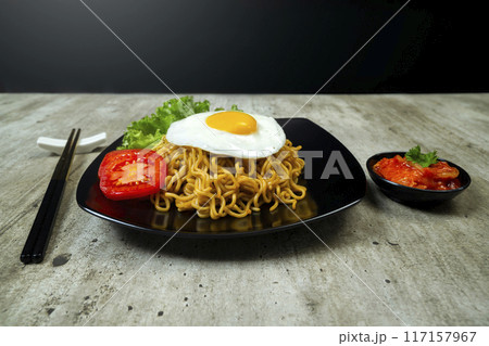 A plate of instant noodles with an egg on top and a tomato slice 117157967