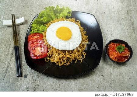 A plate of instant noodles with an egg on top and a tomato slice 117157968