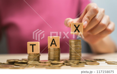 Hand holding wooden cubes with the word TAX on a pile of gold coins. Hand holding wooden cubes with the word TAX on a pile of gold coins. 117158075