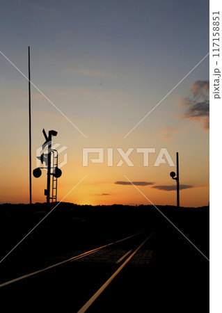 夕陽を浴びて光る線路と警報機 小高い丘のシルエット 夕陽を浴びて光る線路と警報機 小高い丘のシルエット 117158851