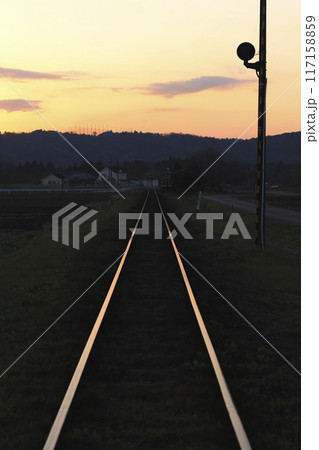 夕陽を浴びて光る線路と小高い丘のシルエット 夕陽を浴びて光る線路と小高い丘のシルエット 117158859