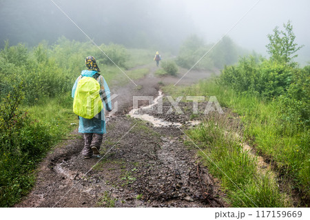 Tourist in raincoat hikes to mountain in the fog Tourist in raincoat hikes to mountain in the fog 117159669