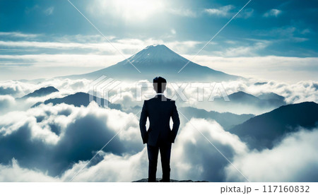 高い目標を定めるイメージ。山の頂上に立ち、より高い山を見つめるビジネスマンの後ろ姿のシルエット。 117160832