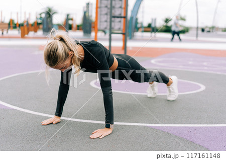 A woman athlete stands in a plank on the sports ground during a workout.	 117161148