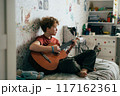 Romantic adolescent redhead girl learning to play the guitar while sitting in the room.	 117162361