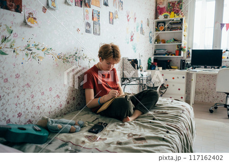 Teenage girl doing homework while sitting in the room.	 117162402