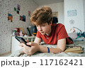 A teenage girl lying on a bed in a room uses a mobile phone for online communication.	 117162421
