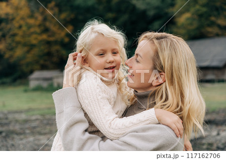 Mom holds in her arms and hugs a little blond cheerful daughter.	 117162706