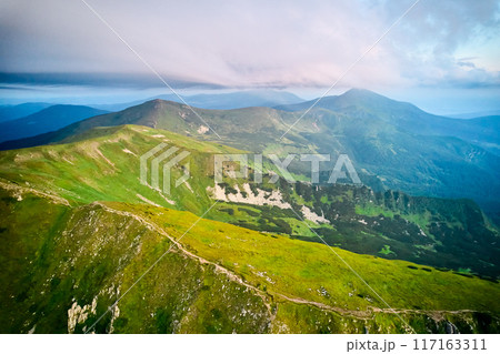 Breathtaking aerial view of green, rugged mountain peaks under dramatic sky. Scene captures contrast between vibrant landscape and moody clouds, with sunlight breaking through. Carpathians, Chornogora Breathtaking aerial view of green, rugged mountain peaks under dramatic sky. Scene captures contrast between vibrant landscape and moody clouds, with sunlight breaking through. Carpathians, Chornogora 117163311