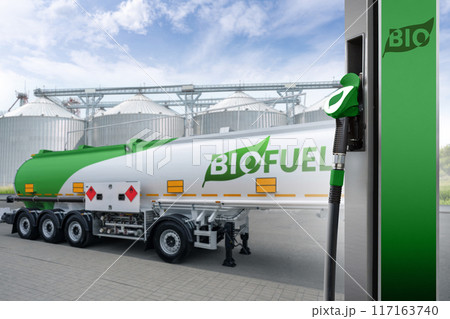 Fuel nozzle with inscription BIO on a background of tank trailer with biofuel. Carbon neutral bio fuel decarbonization concept Fuel nozzle with inscription BIO on a background of tank trailer with biofuel. Carbon neutral bio fuel decarbonization concept 117163740