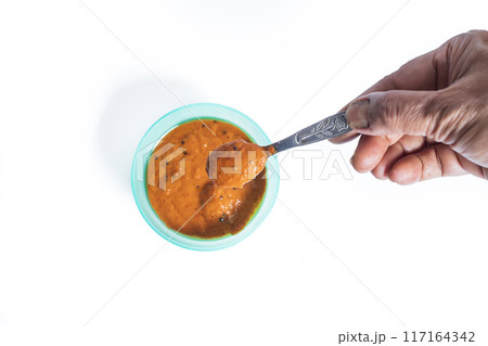 Hand holding spoon with onion chutney on white background with onion chutney in bowl behind. Top view Hand holding spoon with onion chutney on white background with onion chutney in bowl behind. Top view 117164342