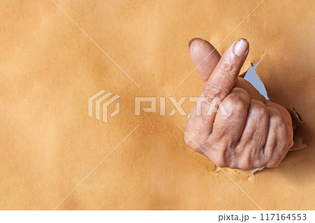 Indian woman hand showing symbol korean mini heart gesture through the torn holes of brown paper background. Indian woman hand showing symbol korean mini heart gesture through the torn holes of brown paper background. 117164553
