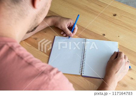 Man Writing in Notebook at Wooden Desk. International Left Handers Awareness Day Man Writing in Notebook at Wooden Desk. International Left Handers Awareness Day 117164783
