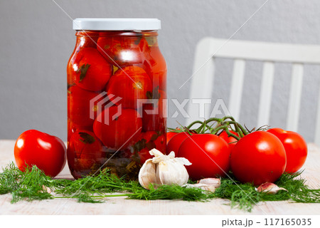 Glass jar with canned tomatoes, ripe tomatoes, garlic and dill on table 117165035