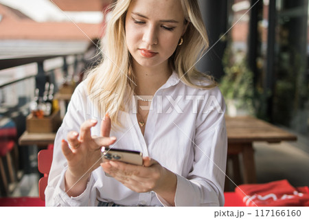 Restaurant and smartphone. Close-up relaxed blond woman typing and scroll or check email and contact social media app or social network user. Happy smile and young gen z girl with mobile tech post to Restaurant and smartphone. Close-up relaxed blond woman typing and scroll or check email and contact social media app or social network user. Happy smile and young gen z girl with mobile tech post to 117166160