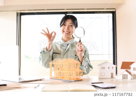 住宅模型の前で虫眼鏡を持つ作業服姿の女性 117167782