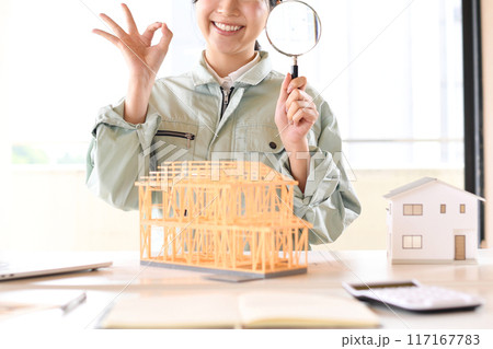 住宅模型の前で虫眼鏡を持つ作業服姿の女性 117167783